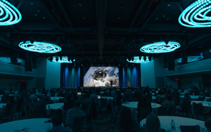 conference hosted in ballroom with screen and round tables